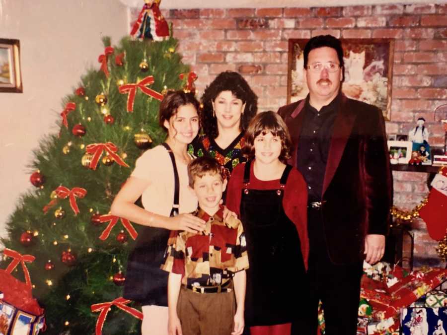 Man who struggled with alcoholism stands in home with wife and three kids beside Christmas tree