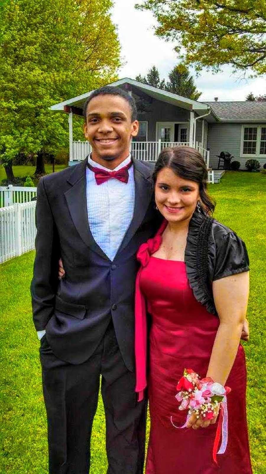 Mixed race high school couple stand smiling outside dressed for prom