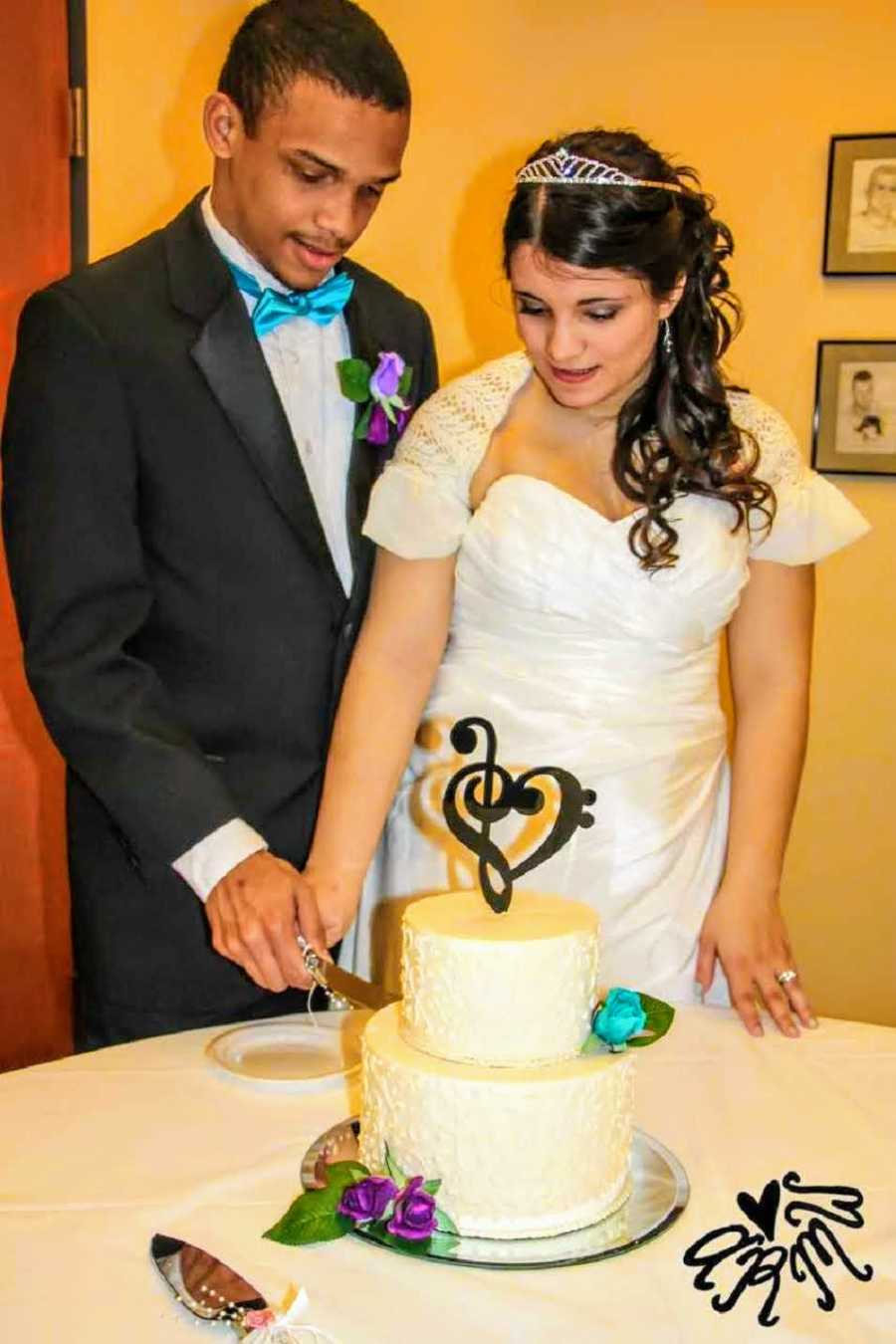 Mixed race bride and groom stand cutting their wedding cake