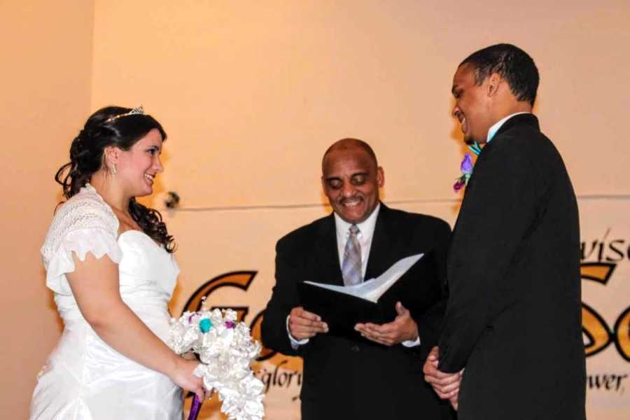 Mixed race bride and groom stand at altar smile beside officiant 