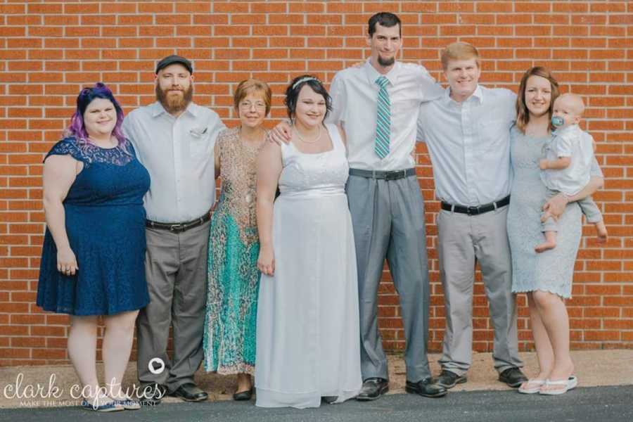 Bride with diabetes stands beside groom and their two families in front of brick wall