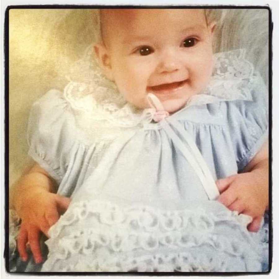 Baby with diabetes sits smiling in christening dress
