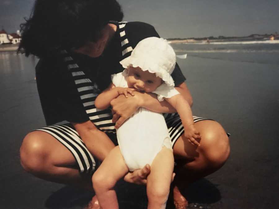 Mother squats on beach as she holds baby with Spinal Muscular Atrophy