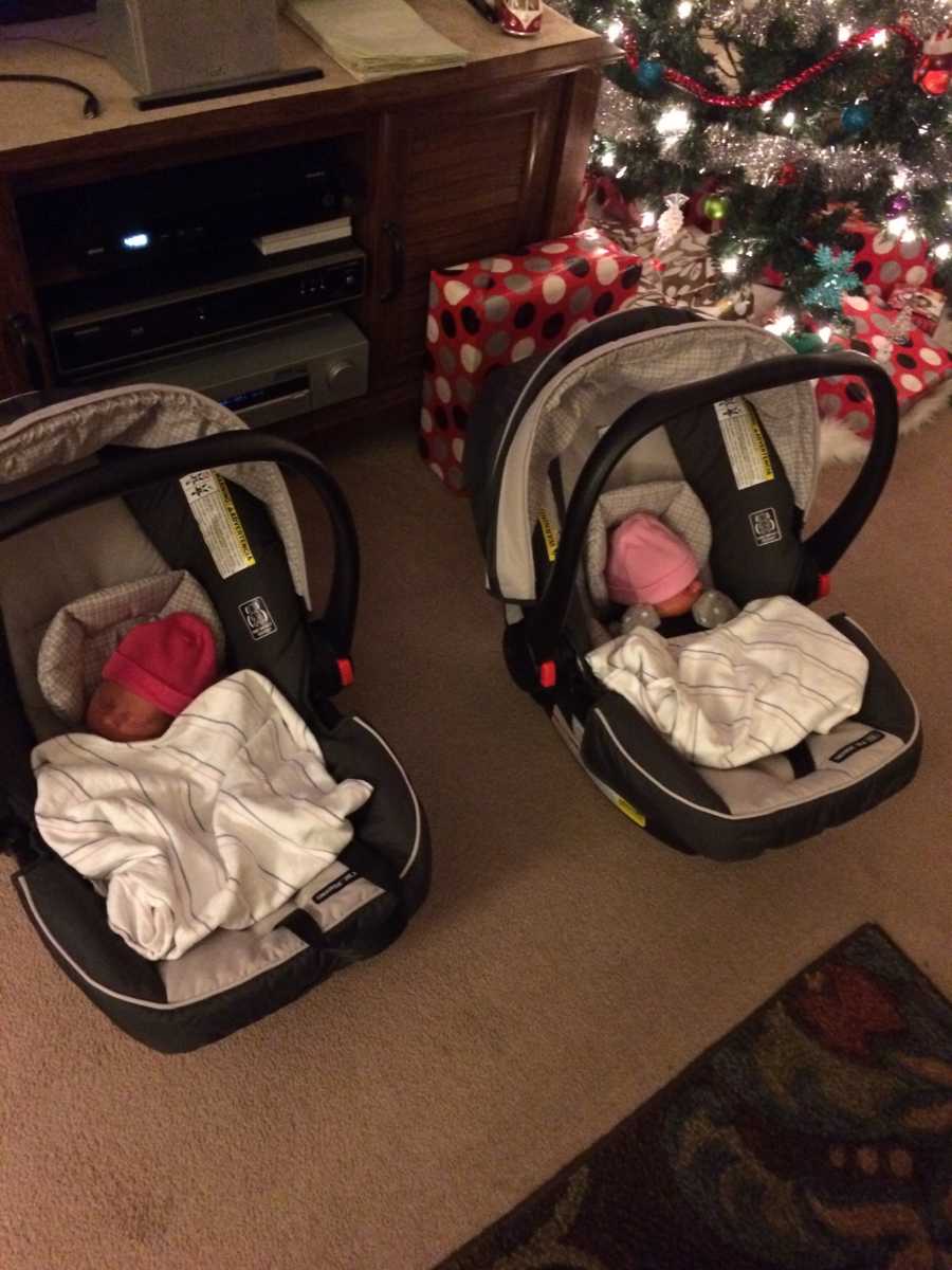 Newborn twins lay asleep in car seat in home beside Christmas tree