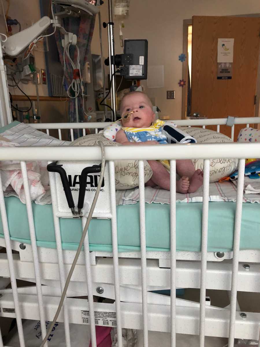 Intubated baby with cancer sits in crib in hospital room