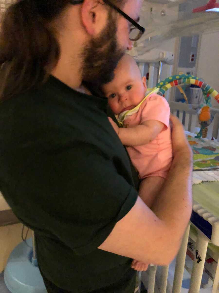 Father stands in hospital holding baby girl with tumor
