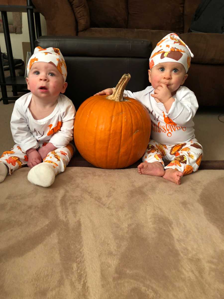 Twin baby girls with cancer sit on floor in home beside pumpkin