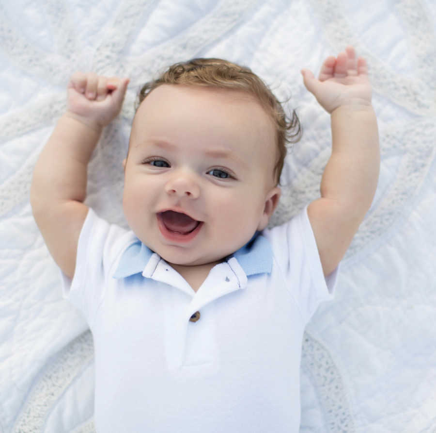 Baby boy with two dads lays on his back smiling with hands in the air