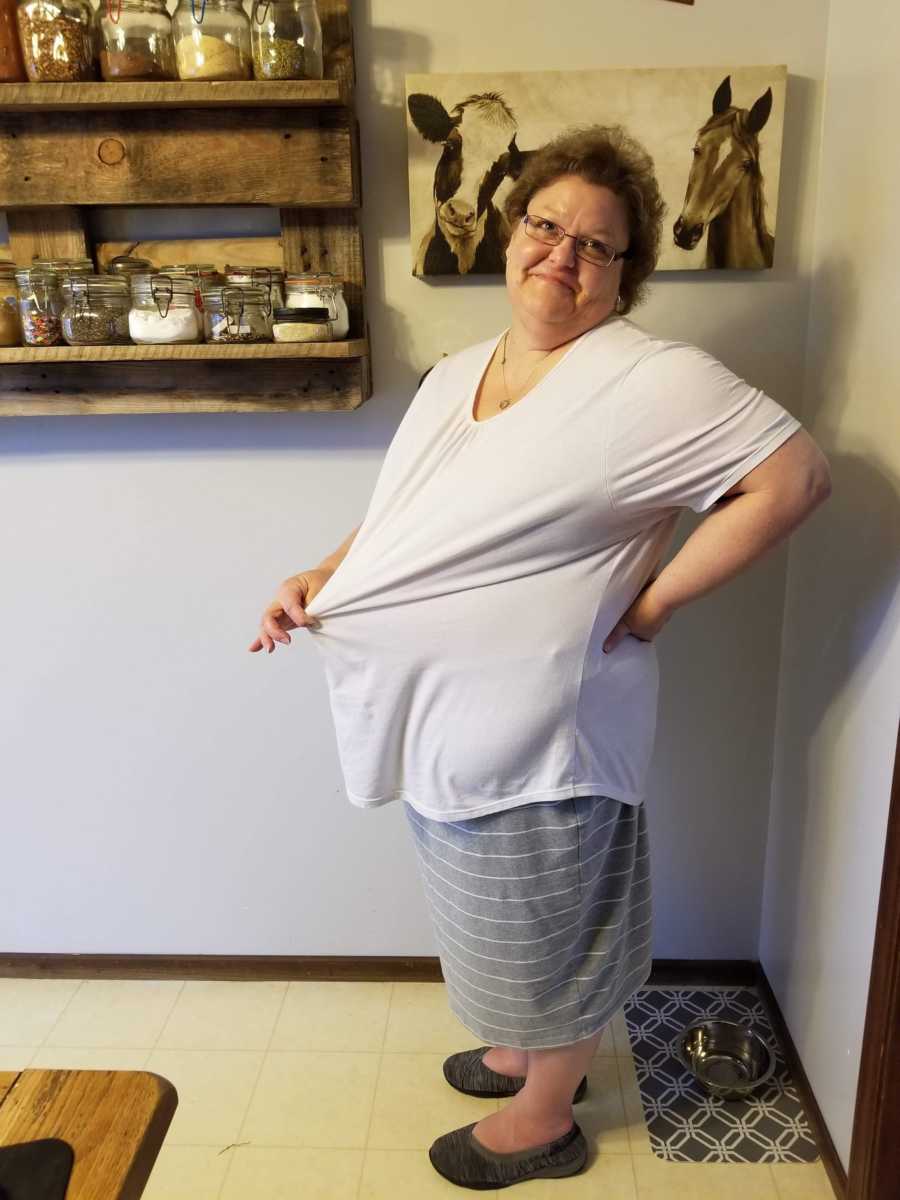Woman with fibromyalgia stands smiling in home wearing shirt that is too big for her after losing weight
