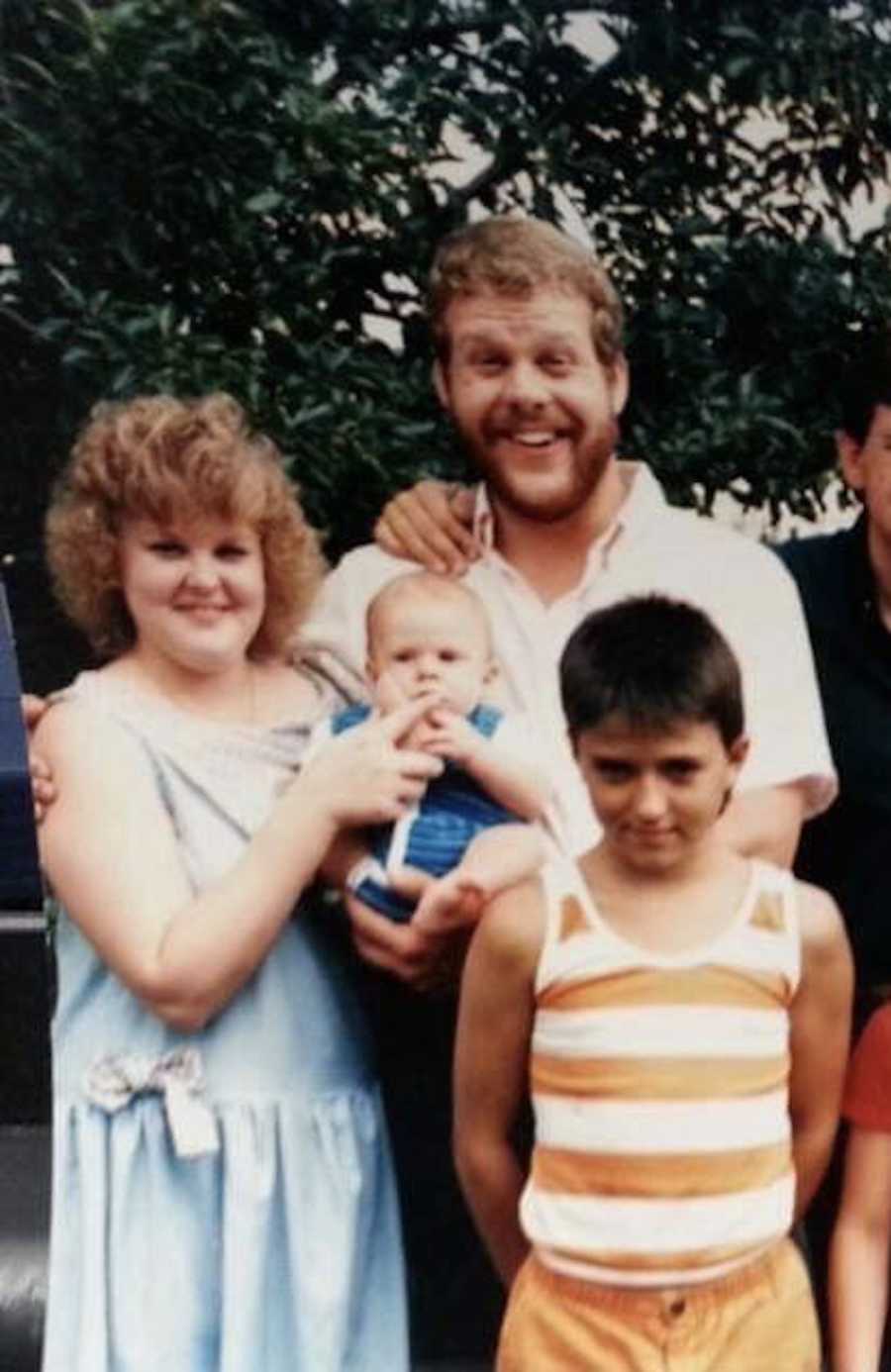 Woman with fibromyalgia stands outside holding baby beside her husband and young boy