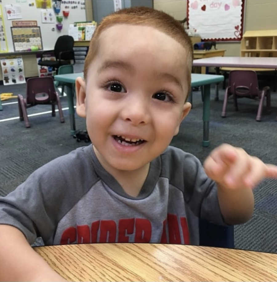 Little boy with Hypotiona smiles as he sits at table in classroom 