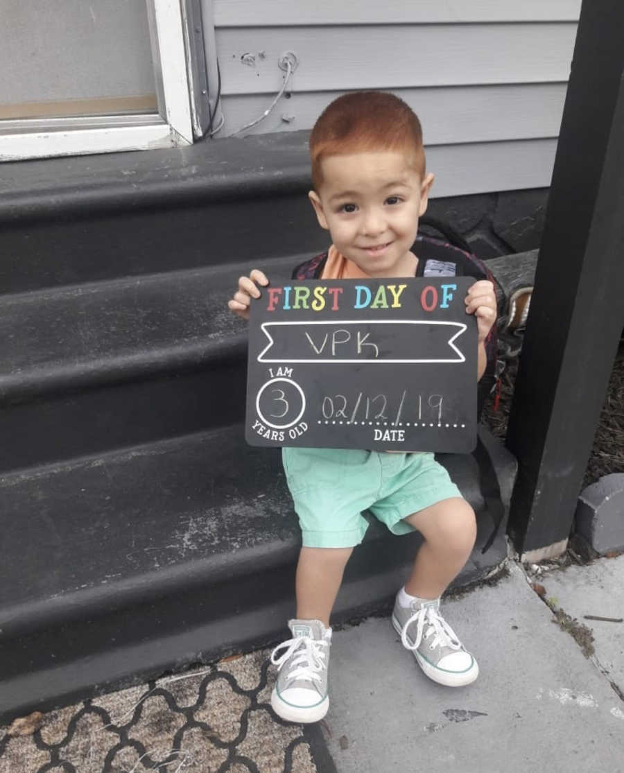 Little boy with Hypotiona sits on outside steps of home holding sign that says, "first day of school"