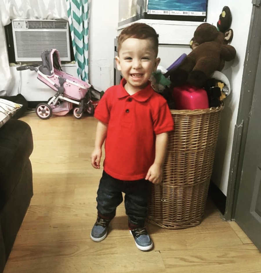 Little boy with Hypotiona stands smiling in home near basket of toys