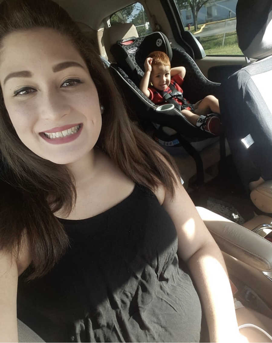 Mother smiles in car with son who has Hypotiona in background sitting in car seat