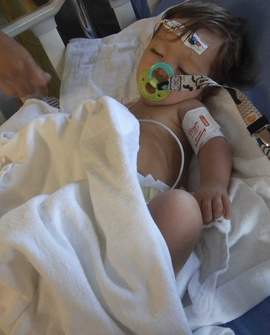 Baby with Hypotiona lays in crib in hospital with pacifier in his mouth and bandage on forehead