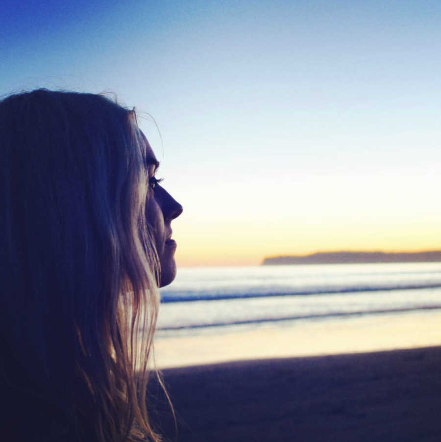 Young woman with POTS disease stands on beach at sunset