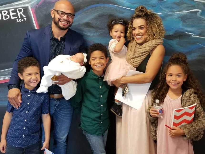 Husband and wife stand smiling with their five children, one of which has down syndrome