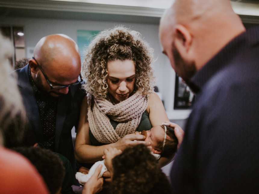 Husband and wife stands in hospital as wife holds baby that might have down syndrome