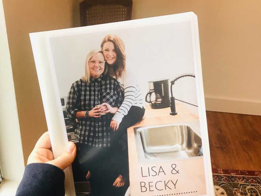 Woman holds photograph of herself and wife as they smile in kitchen 