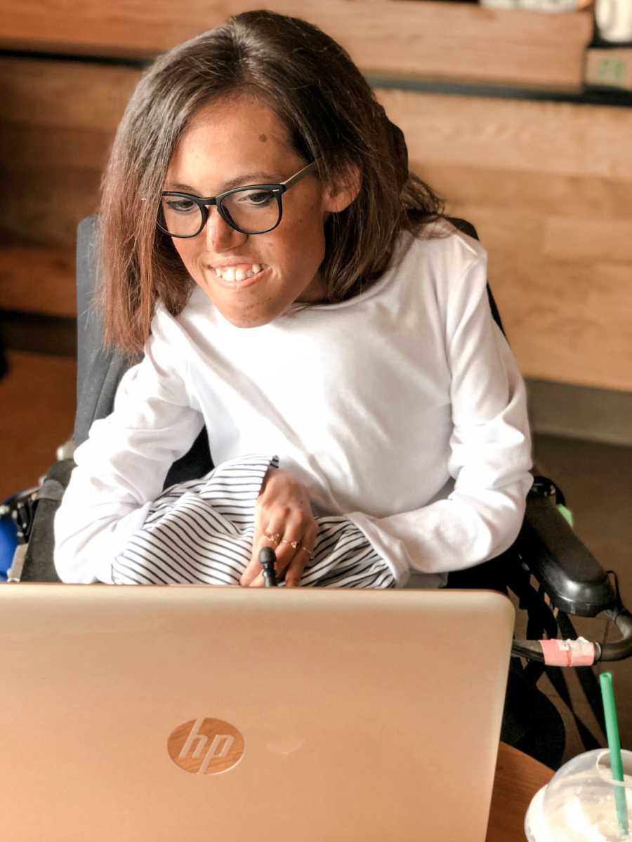 Woman with Spinal Muscular Atrophy sits smiling on computer