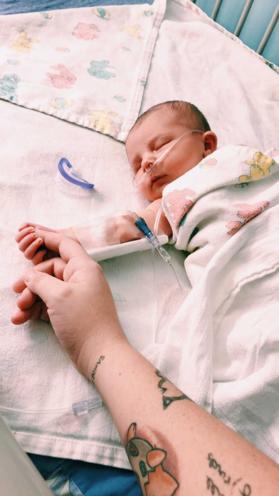 Baby on oxygen lays asleep in crib in NICU while holding mother's finger