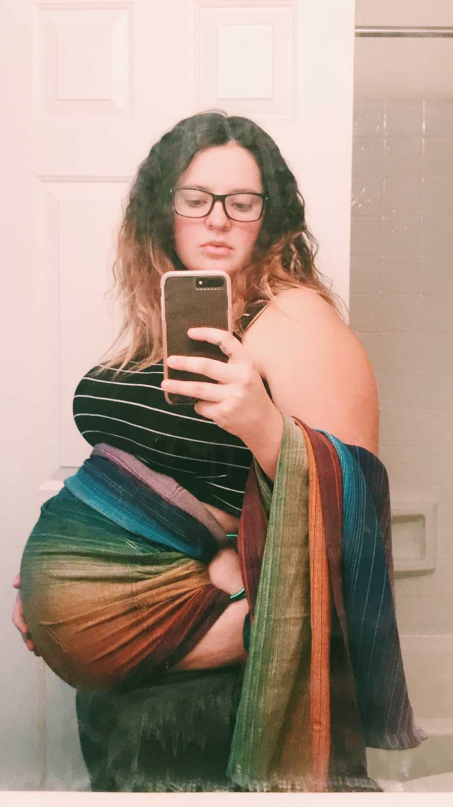 Pregnant woman stands in bathroom taking mirror selfie