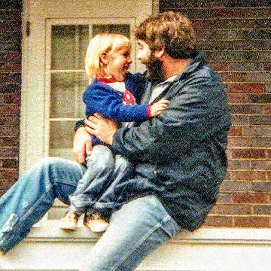 Man sits outside smiling at daughter who sits in his lap smiling back at him