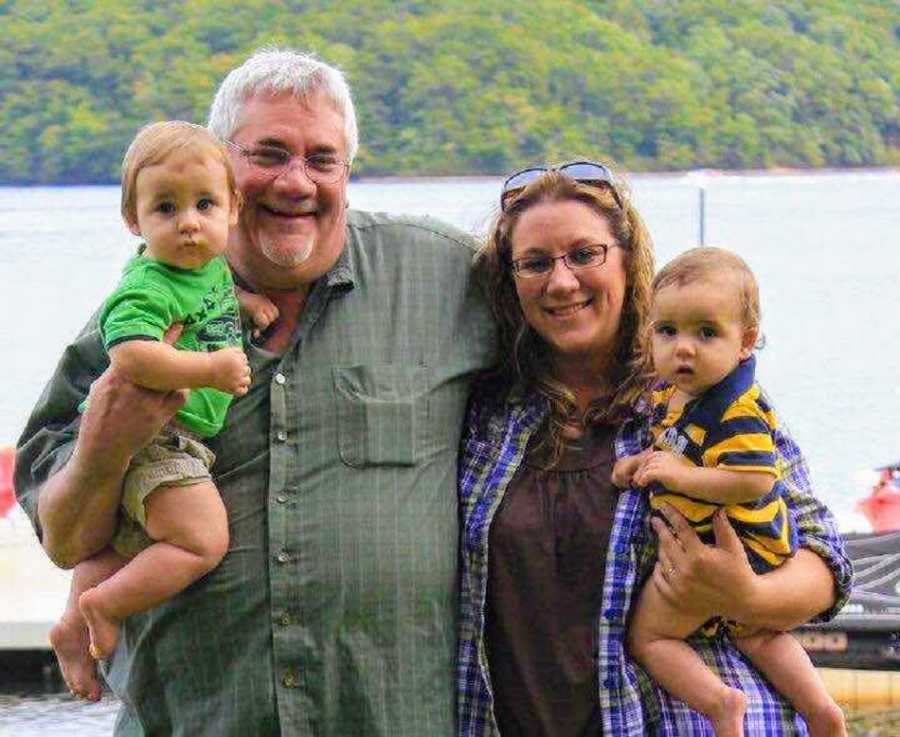 Woman stands outside holding one of her twin sons beside her father who holds the other