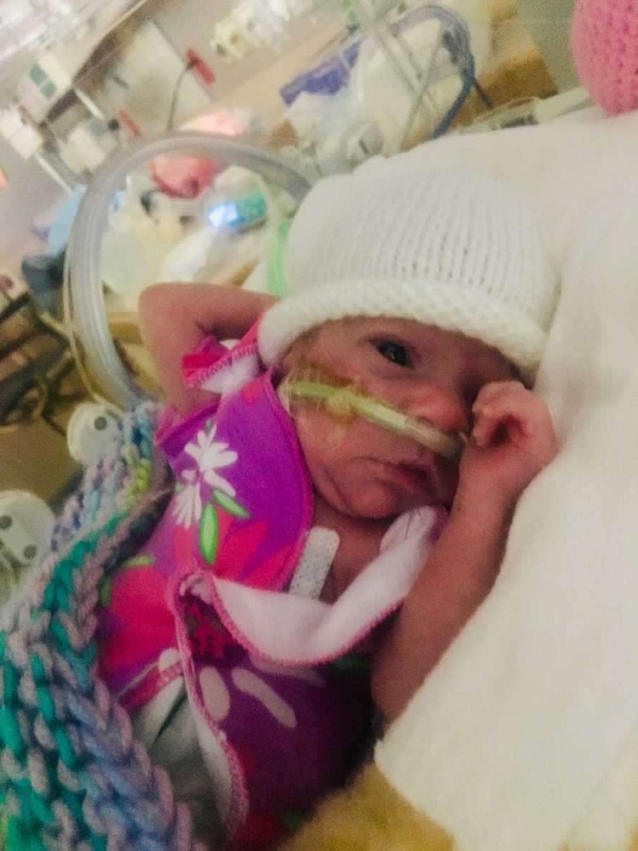 Intubated preemie lays in NICu with knit white hat on