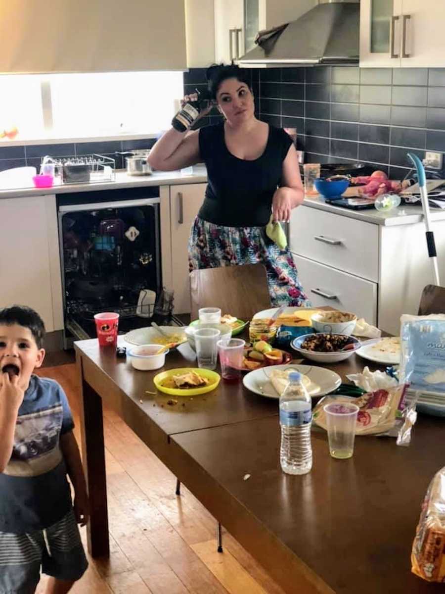 Mother who says she needs some help from husband stands in messy kitchen as he son stands beside messy kitchen table