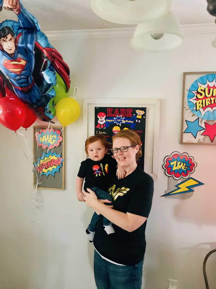 Mother smiles as she holds baby boy in home decorated with super heroes for his first birthday
