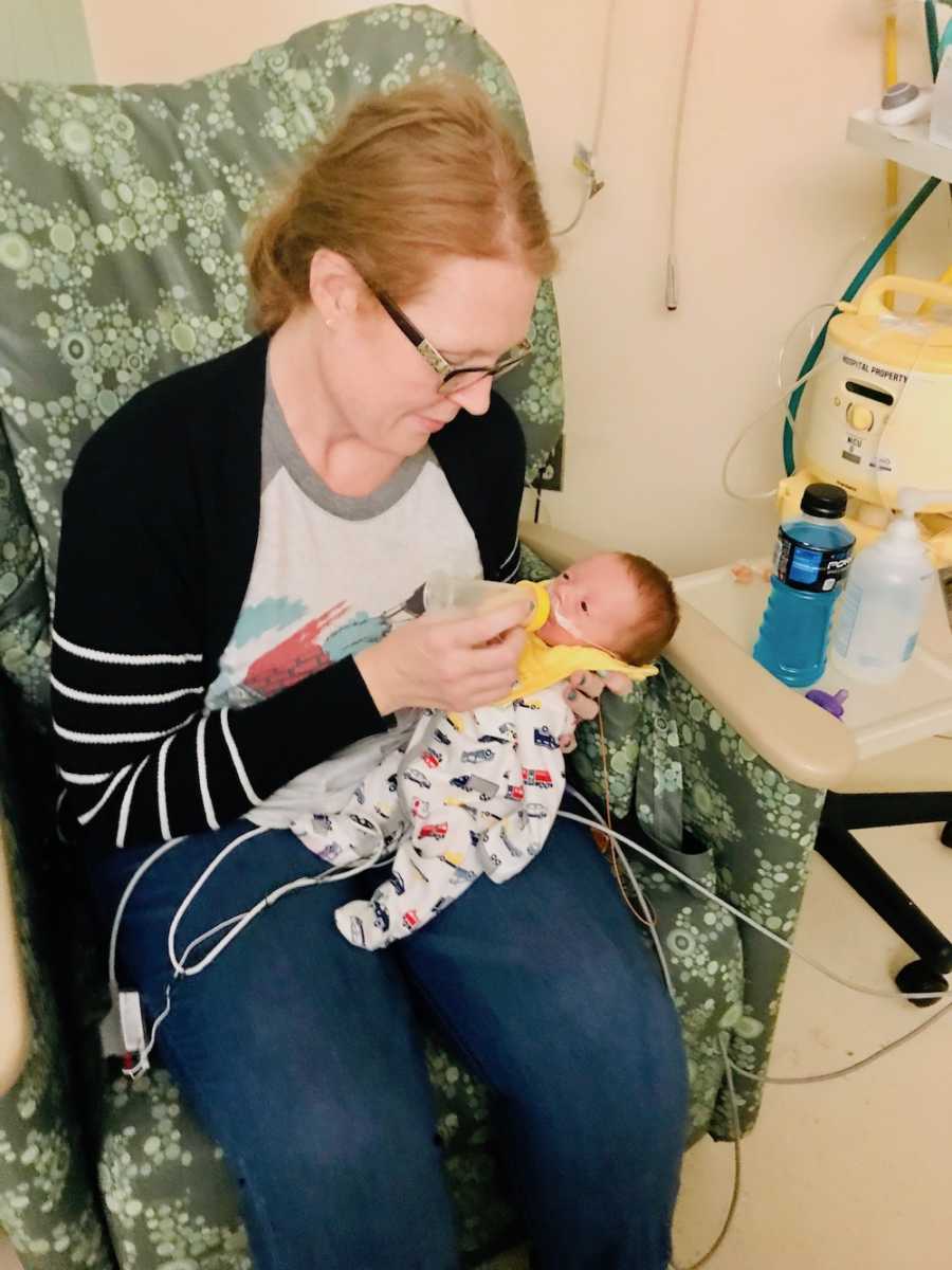 Mother sits in NICU bottle feeding preemie baby in her lap