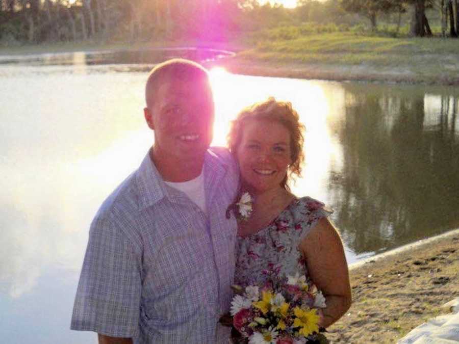 Husband and wife stands smiling beside body of water after their casual wedding