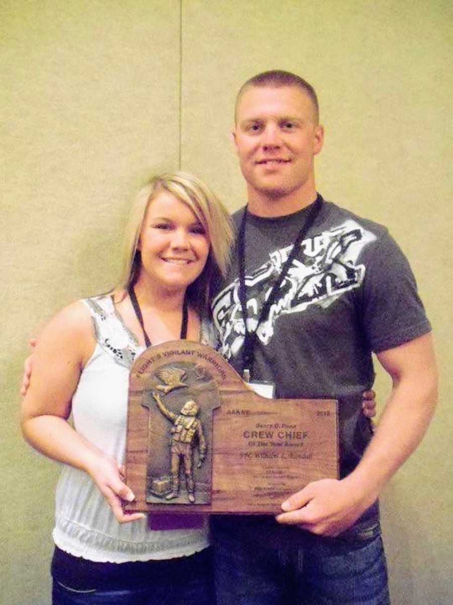 Husband and wife stand smiling as they hold Army Aviation Crew Chief of the Year award husband received 