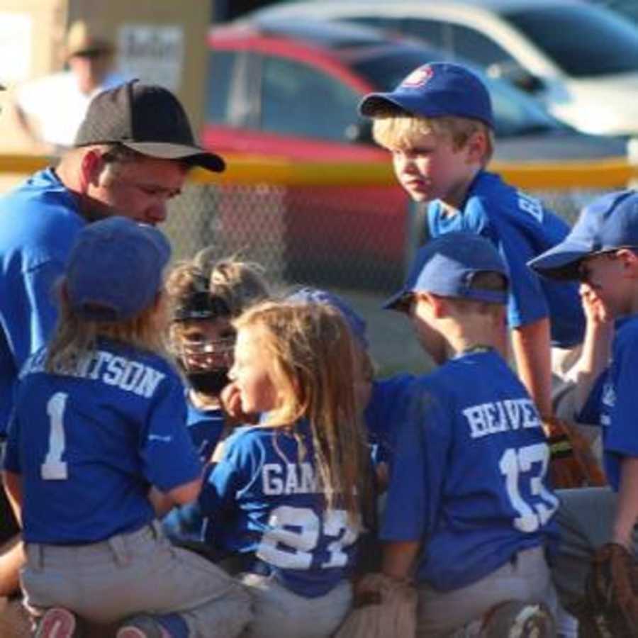 Man who has since passed away sits on ground with little kids who he coaches on baseball team