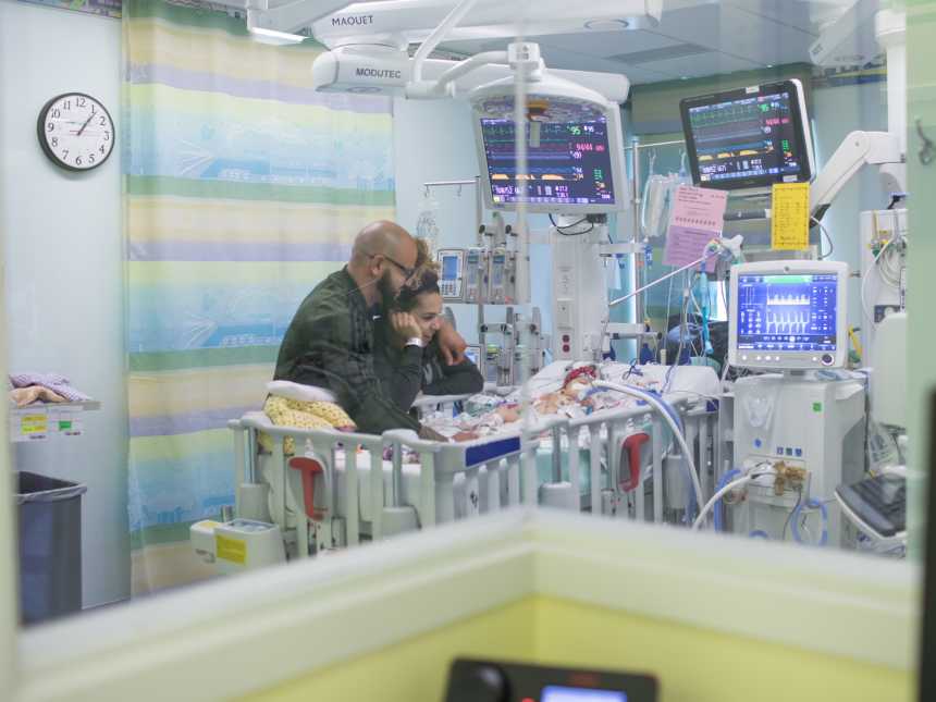 Husband and wife stand over crib in NICU watching their baby