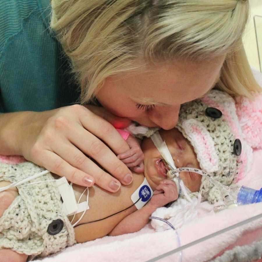 Mother leans over to kiss her intubated newborn baby who lays in NICU