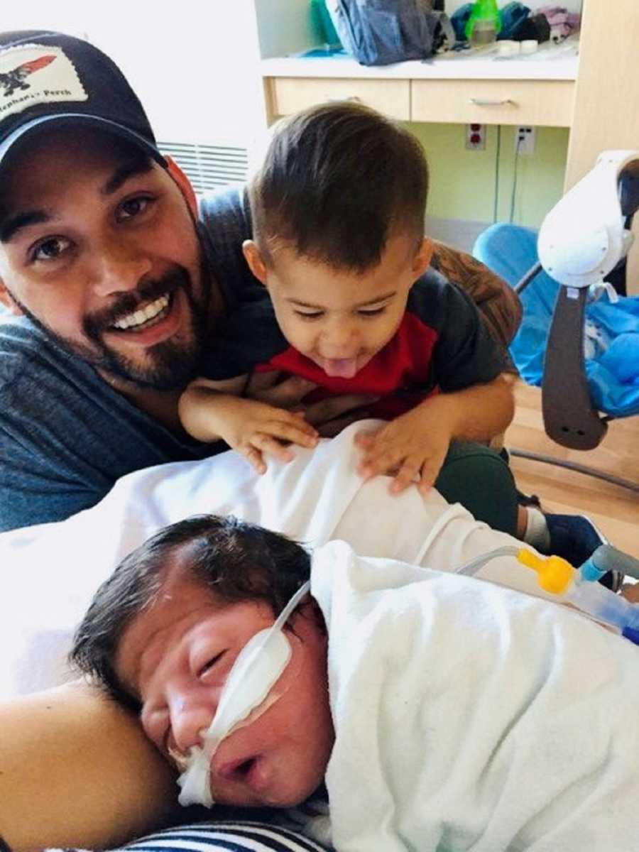 Father smiles as he holds son beside newborn baby on oxygen