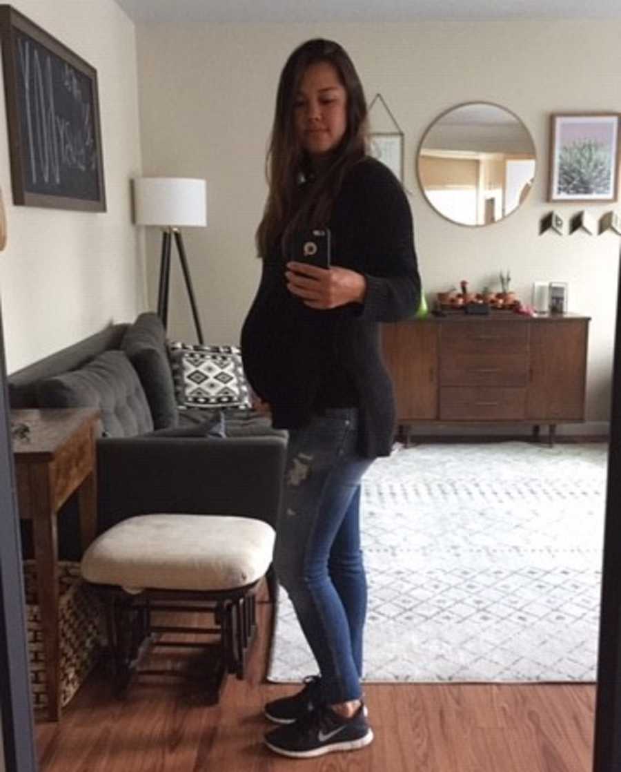 Pregnant woman stands in home taking mirror selfie 