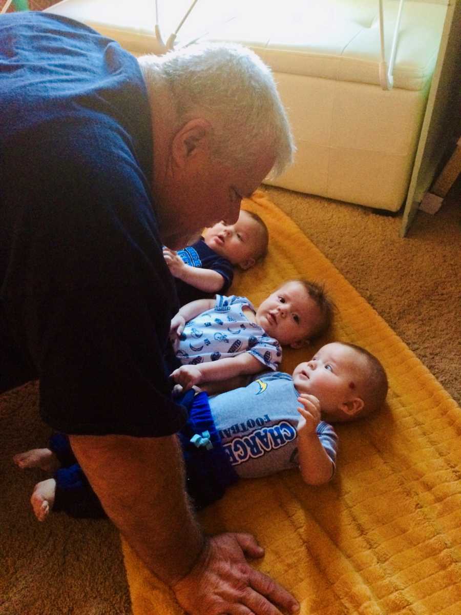 Man kneels over triplet grandchildren who lie on their back on the ground