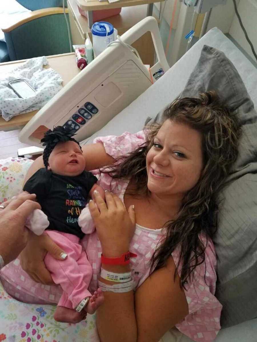 Woman smiles as she lays in hospital bed holding newborn girl