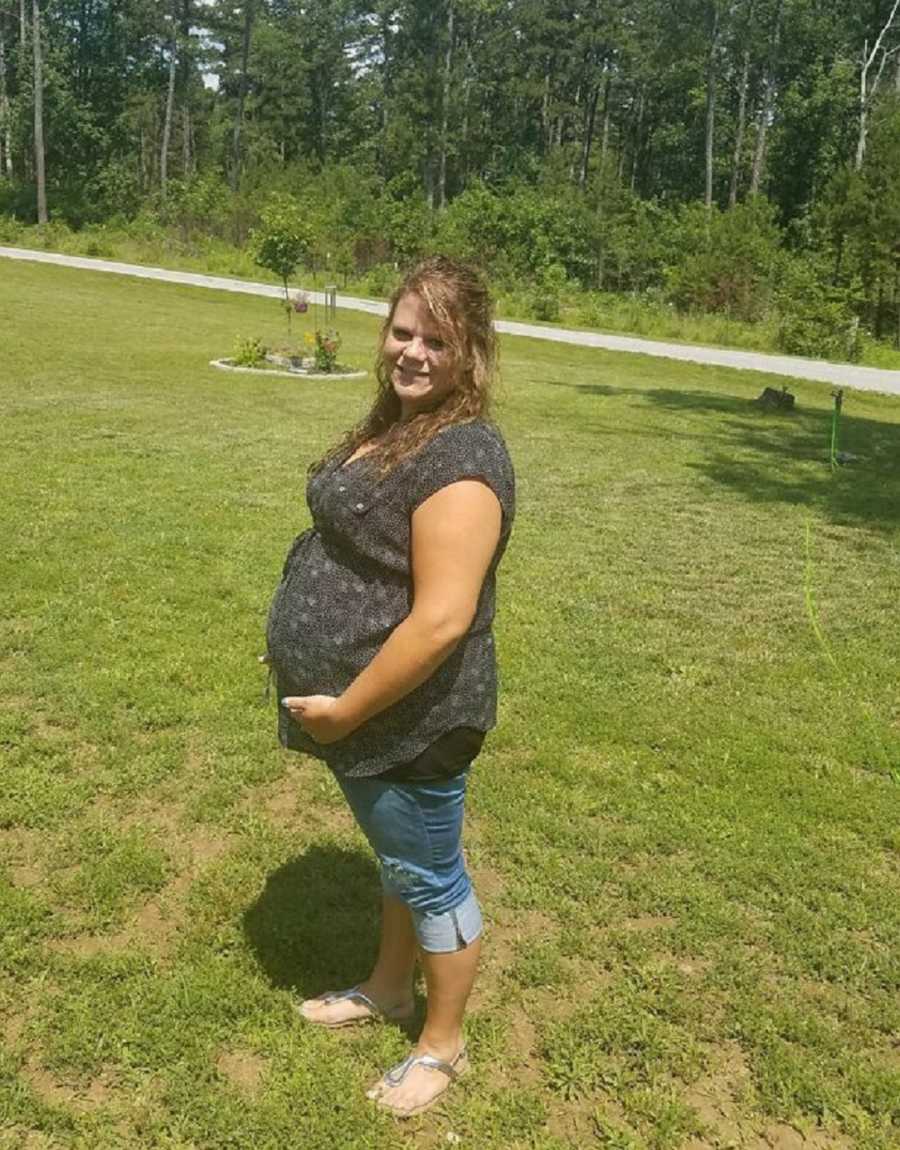 Woman who has always wanted a child stands outside smiling as she holds pregnant stomach