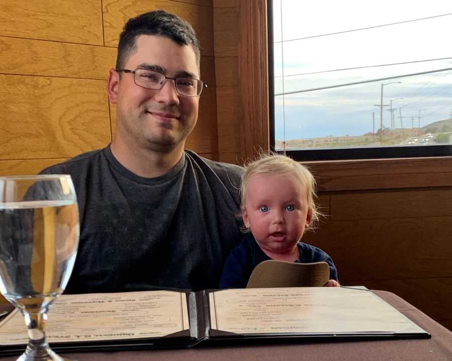 Man sits at restaurant table smiling beside his baby son with Ichthyosis