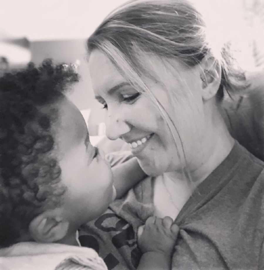 Woman sits as she smiles down at adopted son in her lap