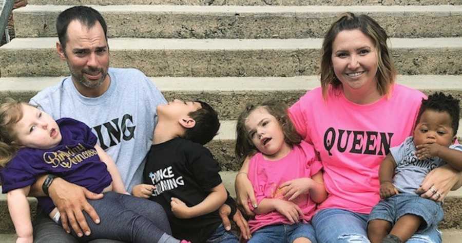 Husband and wife sit on steps outside with their four adopted children in their laps