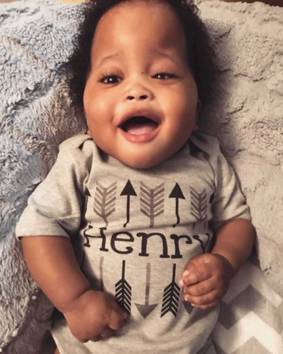 Adopted baby boy lays on his back with his mouth open as he smiles