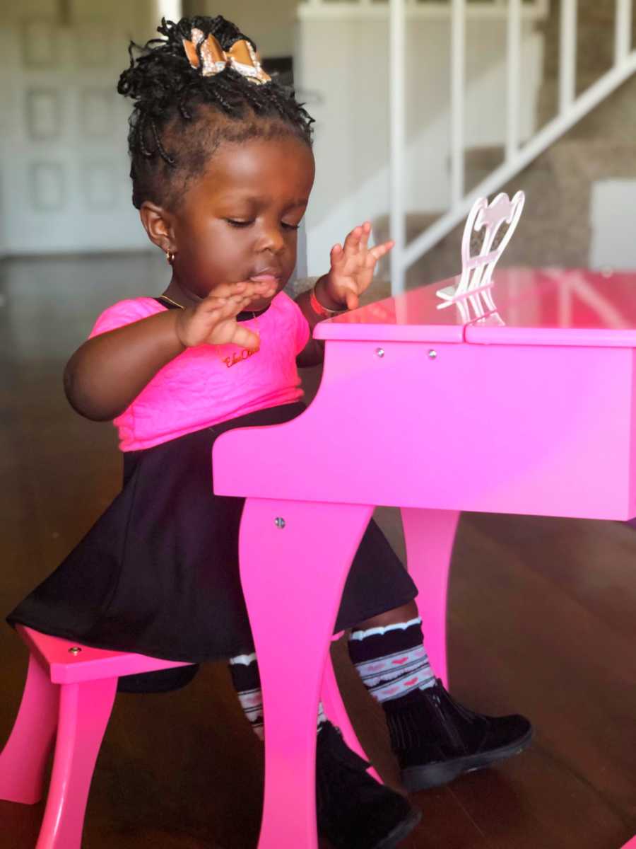 Little girl whose mother almost died giving birth to her sits at small pink piano