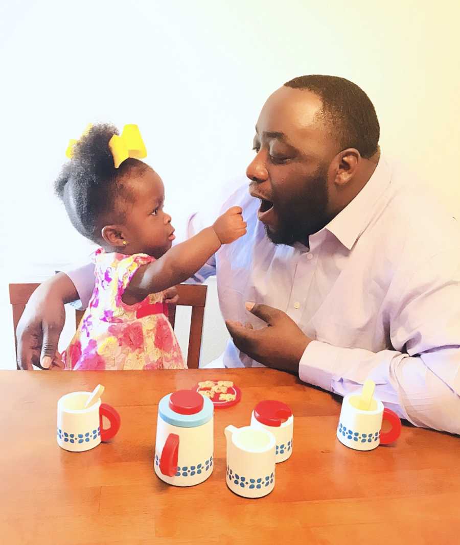 Little girl whose mother almost died giving birth to her sits at table feeding father