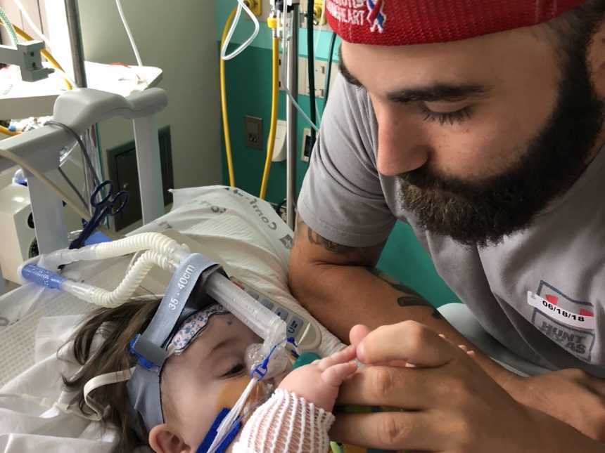 Father holds hand of intubated daughter with down syndrome in PICU