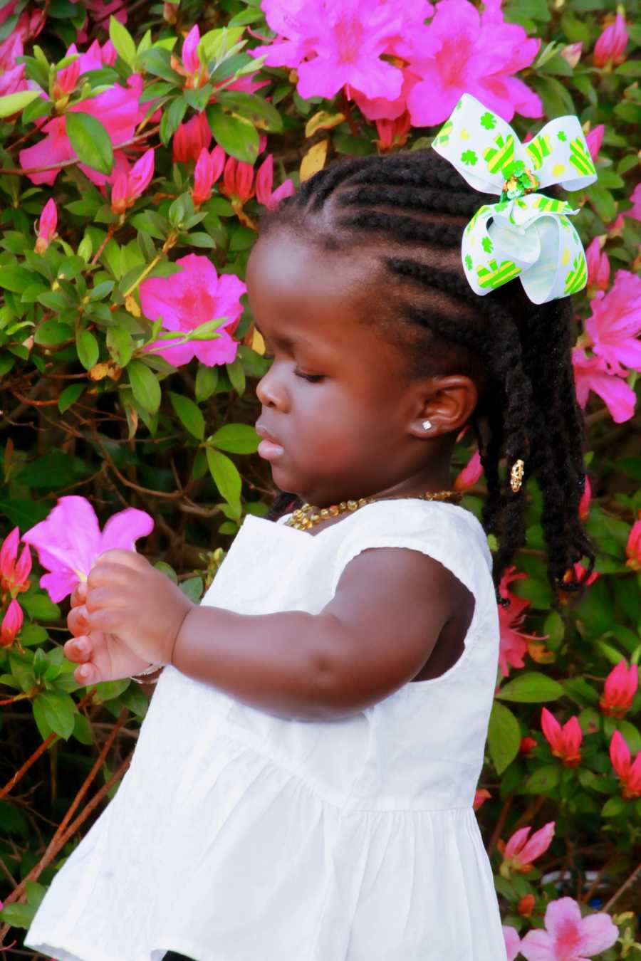 Little girl whose mother almost died giving birth to her stands outside holding pink flower